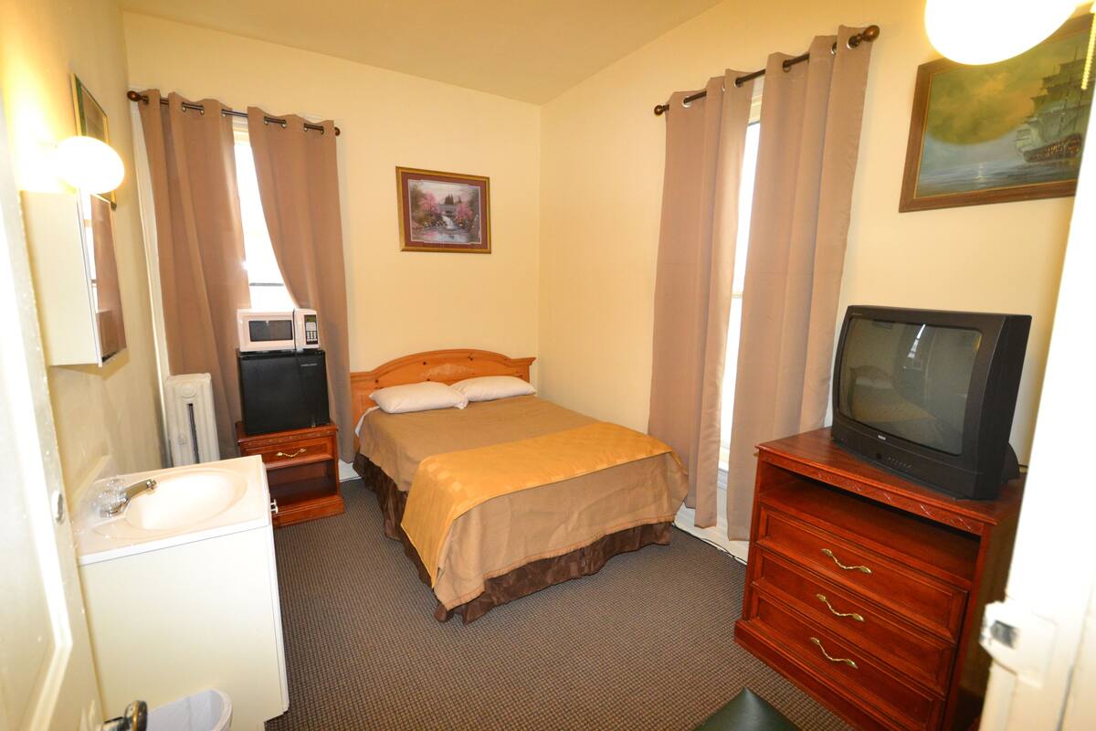A hotel room with a bed, a TV, a dresser, a mirror, a sink, and curtains.