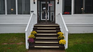 A hotel entrance with a staircase, a sign indicating it's open, and flower arrangements at the base. - Perfect Stay Inn & Suites (Blair)