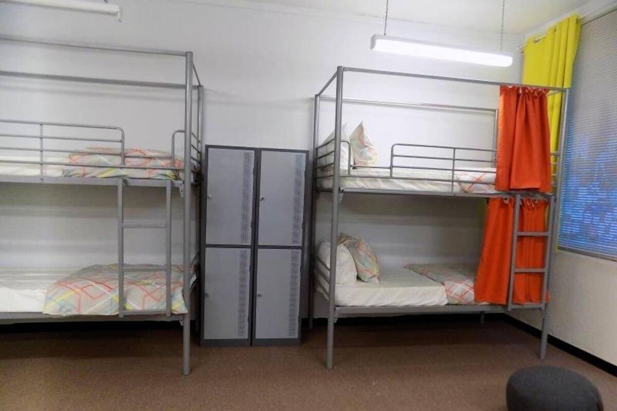 A dormitory room with bunk beds, a wardrobe, and a small stool.