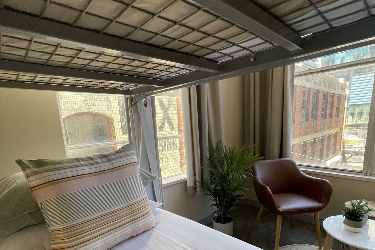 A hotel room with a bed, a chair, a small table, and a potted plant.