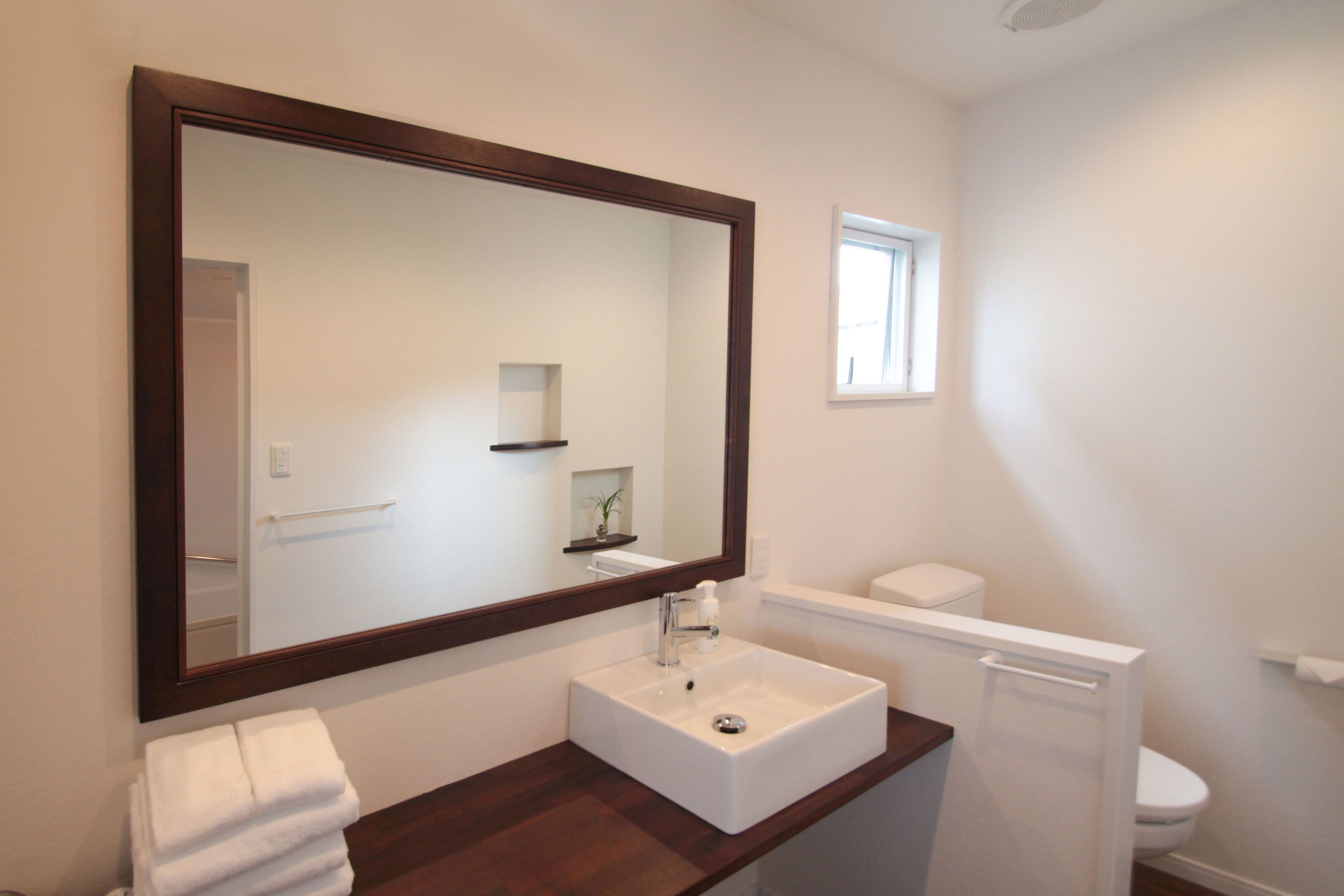 Un baño con un espejo grande, un lavamanos blanco, un inodoro y una ventana pequeña.
