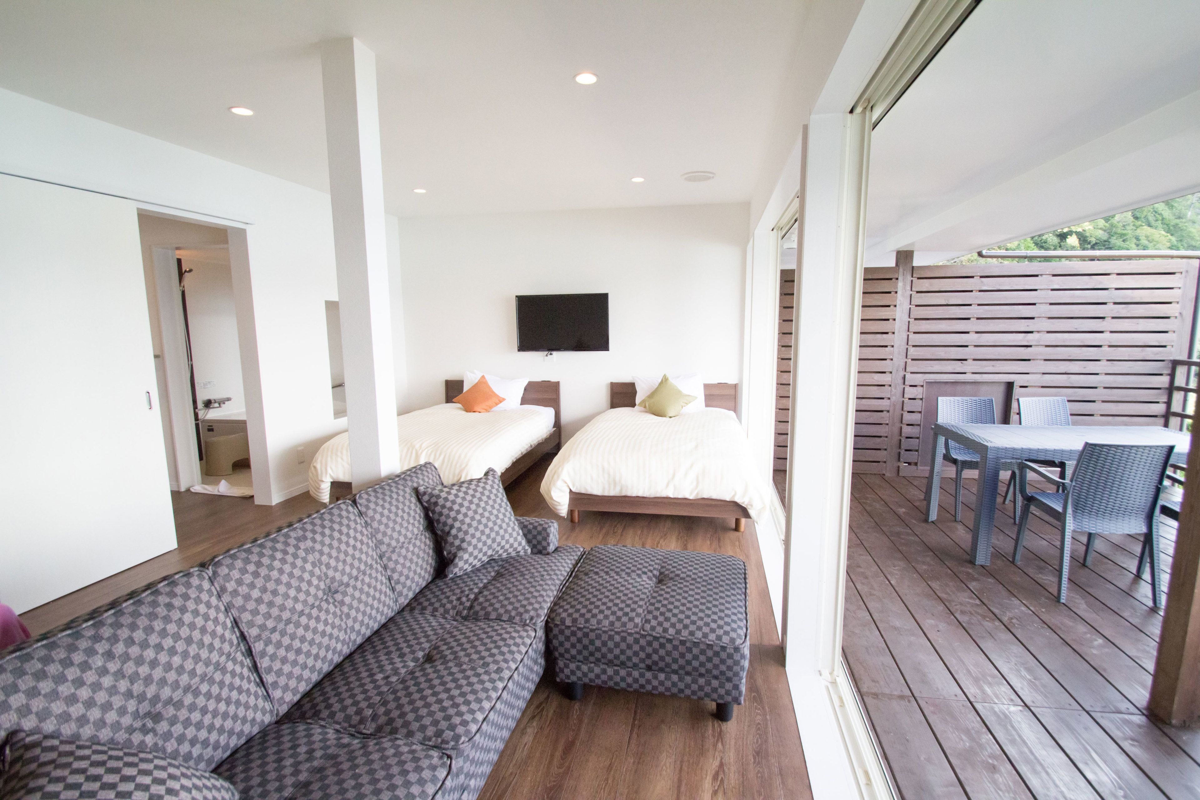 A modern bedroom with two beds, a sofa, and a balcony with a table and chairs.