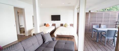 A modern bedroom with two beds, a sofa, and a balcony with a table and chairs.