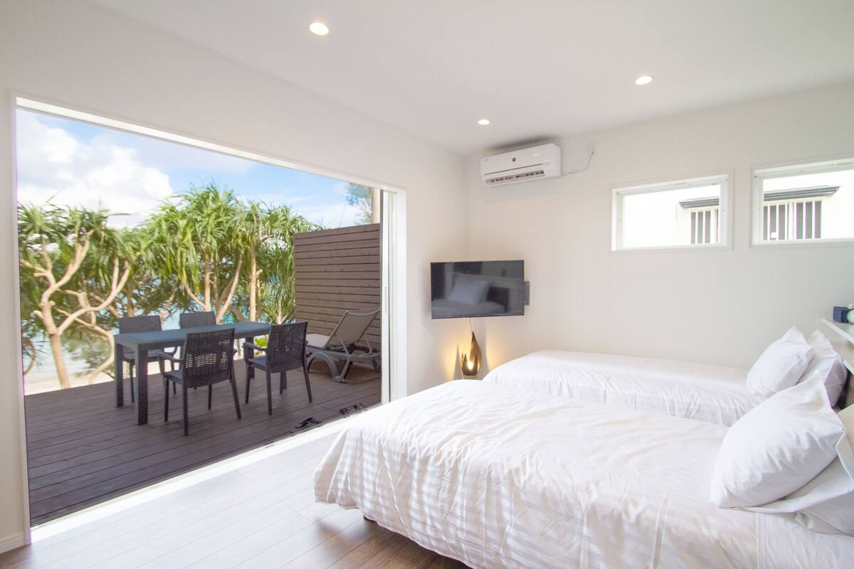 A bedroom with a bed, a TV mounted on the wall, and a balcony with a table and chairs.