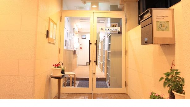 A hotel entrance with a glass door, a small table with a potted plant, and a sign indicating it's a T&K hostel.