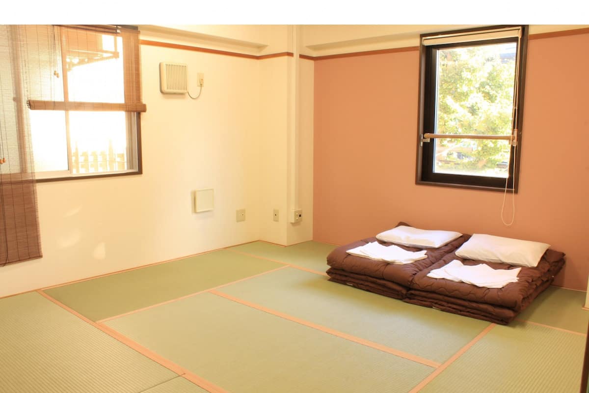 Ein Zimmer mit Tatami-Matten, einem Bett mit Kissen, einem Fenster mit Blick und einer Wandheizung.