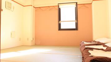 A room with tatami mats, a bed with a brown blanket, a window with a blind, and a radiator on the wall.