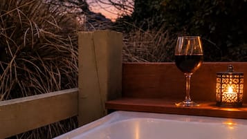 A hot tub with a glass of red wine and a candle, surrounded by wooden benches and plants.