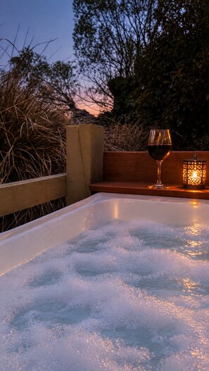 A hot tub with a glass of red wine and a candle, surrounded by wooden benches and plants. - Burn Cottage Retreat (Cromwell)