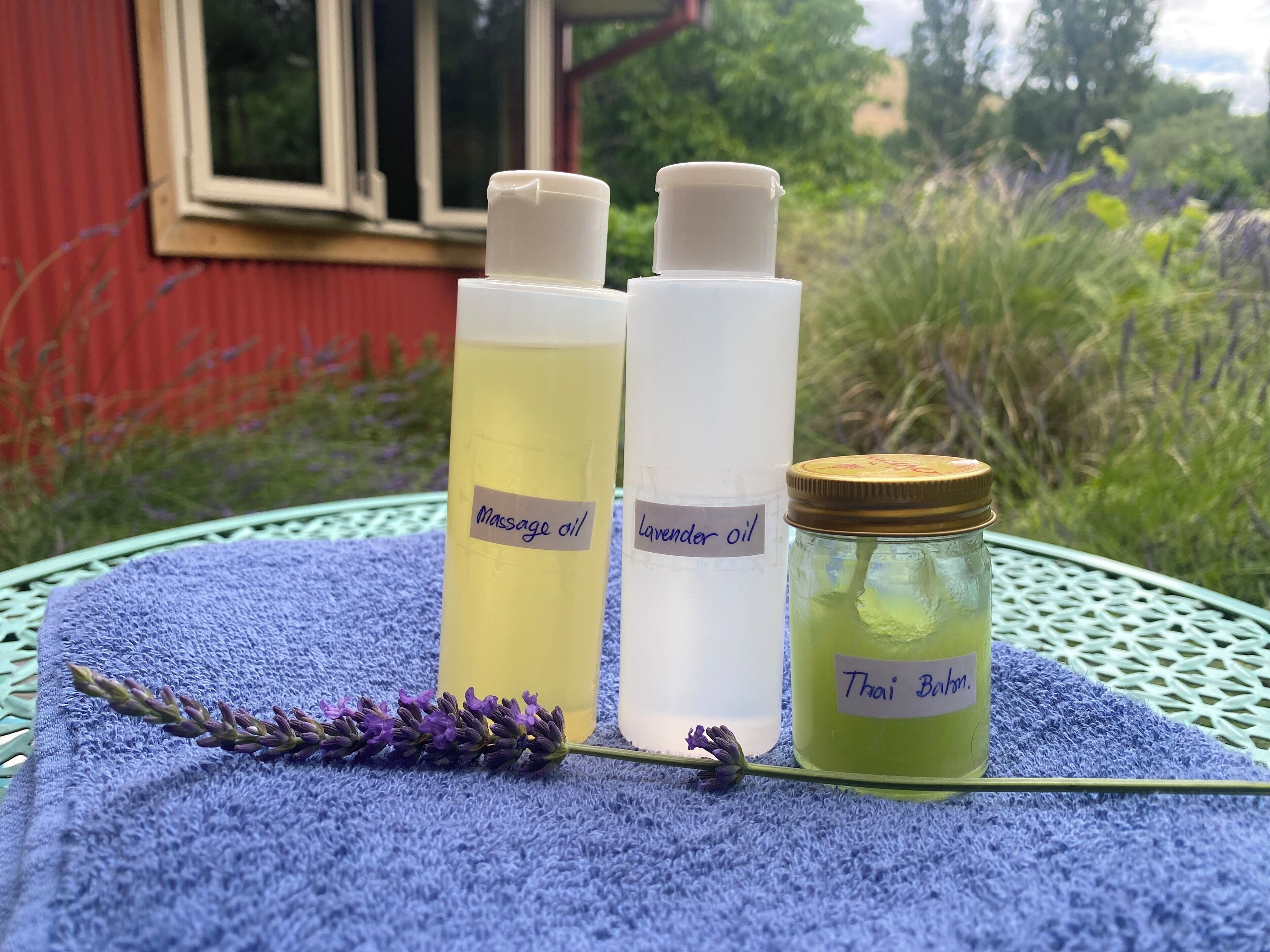 Three bottles of oil on a blue towel with a lavender sprig, placed on a table outdoors.