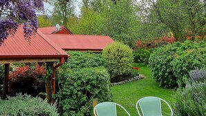 Un jardín con un pérgola, sillas verdes y un edificio de techo rojo.
