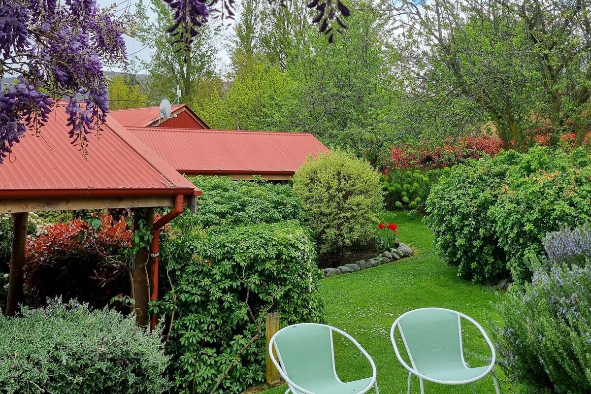A garden with a pergola, green chairs, and a red-roofed building.