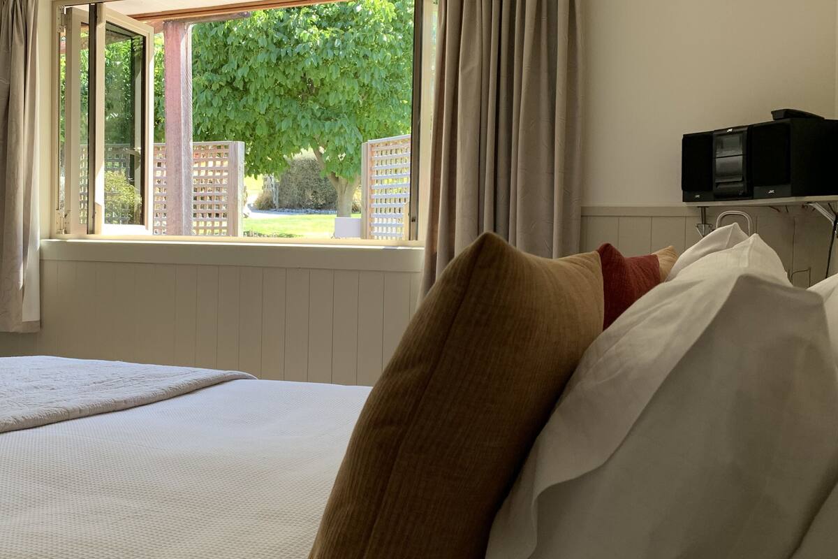 A bedroom with a large bed, a window with curtains, a radiator, and a television on a shelf.