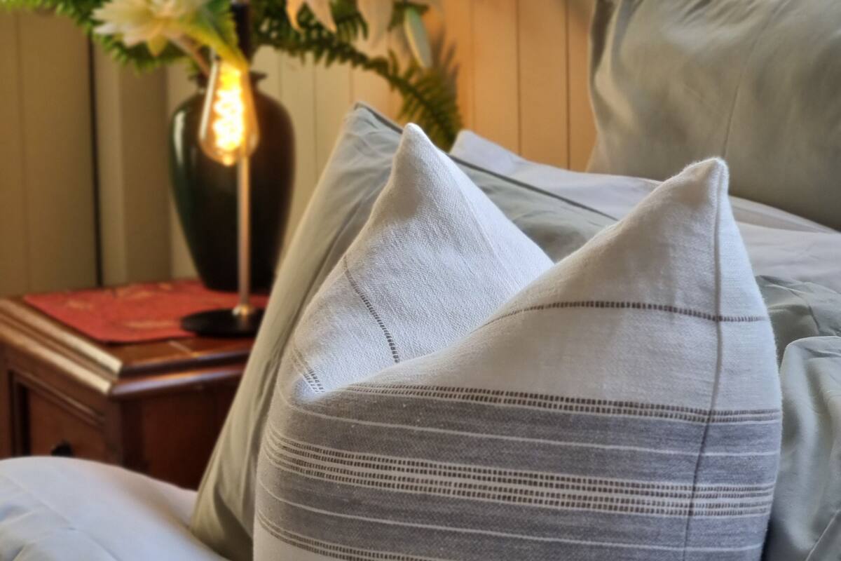 A bed with grey pillows and a vase with flowers on a bedside table.