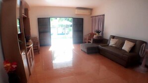 A living room with a sofa, a coffee table, and a TV. There is a sliding door leading to an outdoor area. - Hua Hin Home 66 Pool Villa (Hua Hin)