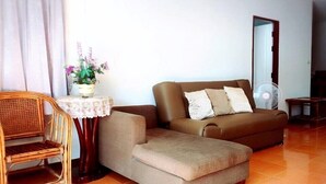 A living room with a brown sofa, a small table with a lace tablecloth, a wicker chair, and a potted plant. - Hua Hin Home 66 Pool Villa (Hua Hin)