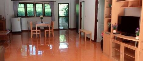 A spacious living area with a dining table, chairs, a bench, a TV stand, and a refrigerator.