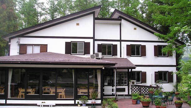 A two-story building with a covered patio area featuring outdoor seating and potted plants.