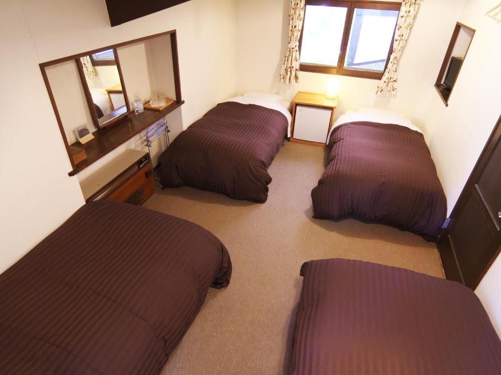 A room with two single beds, a small bedside table, a mirror, and a window with curtains.
