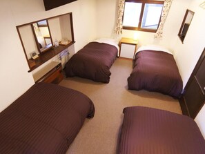 A room with two single beds, a small bedside table, a mirror, and a window with curtains.