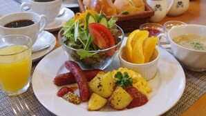 A breakfast setting with a plate of sausages, potatoes, scrambled eggs, and a salad. There are also cups of coffee and orange juice, a basket of bread, and a teapot.