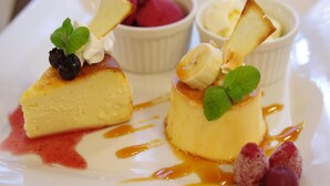 A dessert plate with two flan cakes topped with banana slices, mint leaves, and berries, accompanied by a scoop of ice cream and a small bowl of berries.