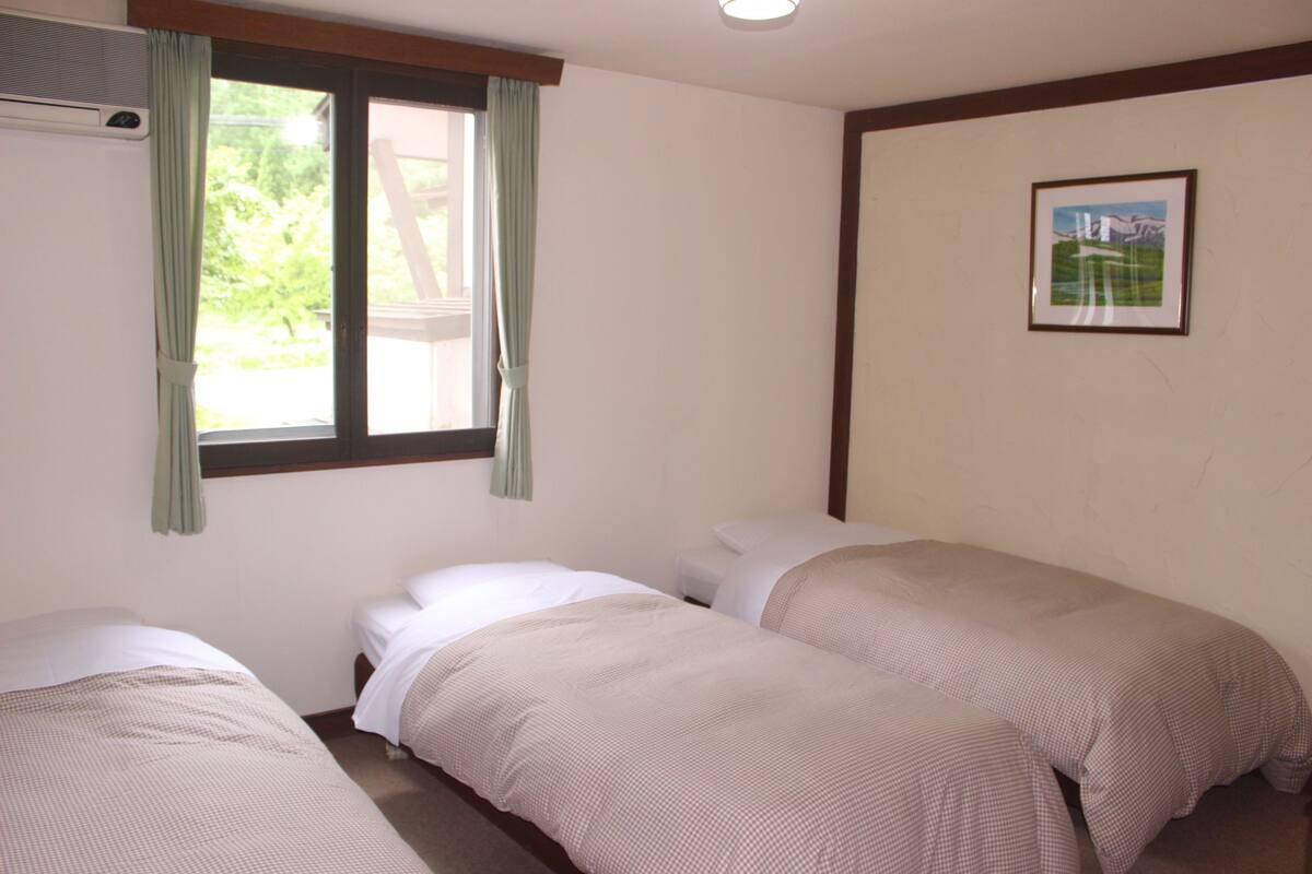 Una habitación con dos camas individuales, una ventana con cortinas, un aire acondicionado de pared y un cuadro enmarcado.