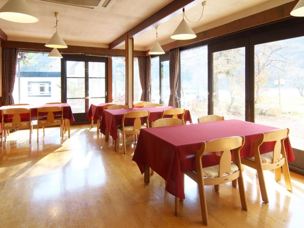 A dining area with tables and chairs, large windows, and a wooden floor.