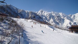 A ski slope with skiers, a chairlift, and snow-covered mountains.