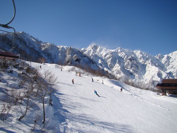 A ski slope with skiers, a chairlift, and snow-covered mountains.