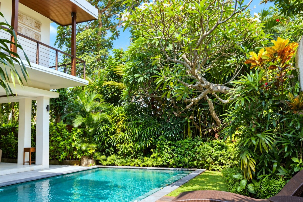 A poolside area with a modern house, lush greenery, and a clear blue pool.