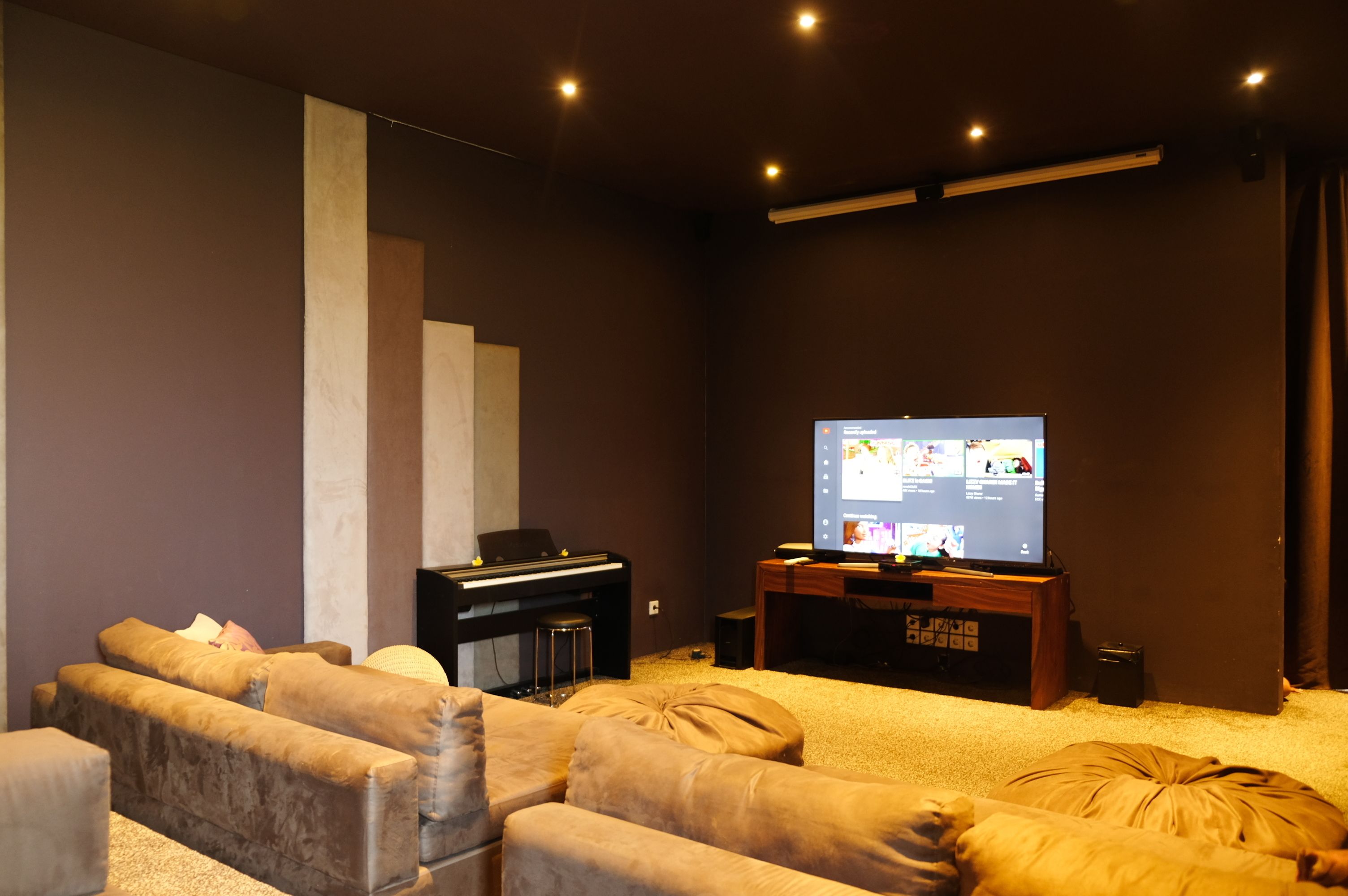 A modern home theater with a large flat-screen TV, a piano, and comfortable seating.
