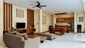 A modern living room with a flat-screen TV, a sofa, a coffee table, and a dining area with a bench. - Villa Sally (Canggu)