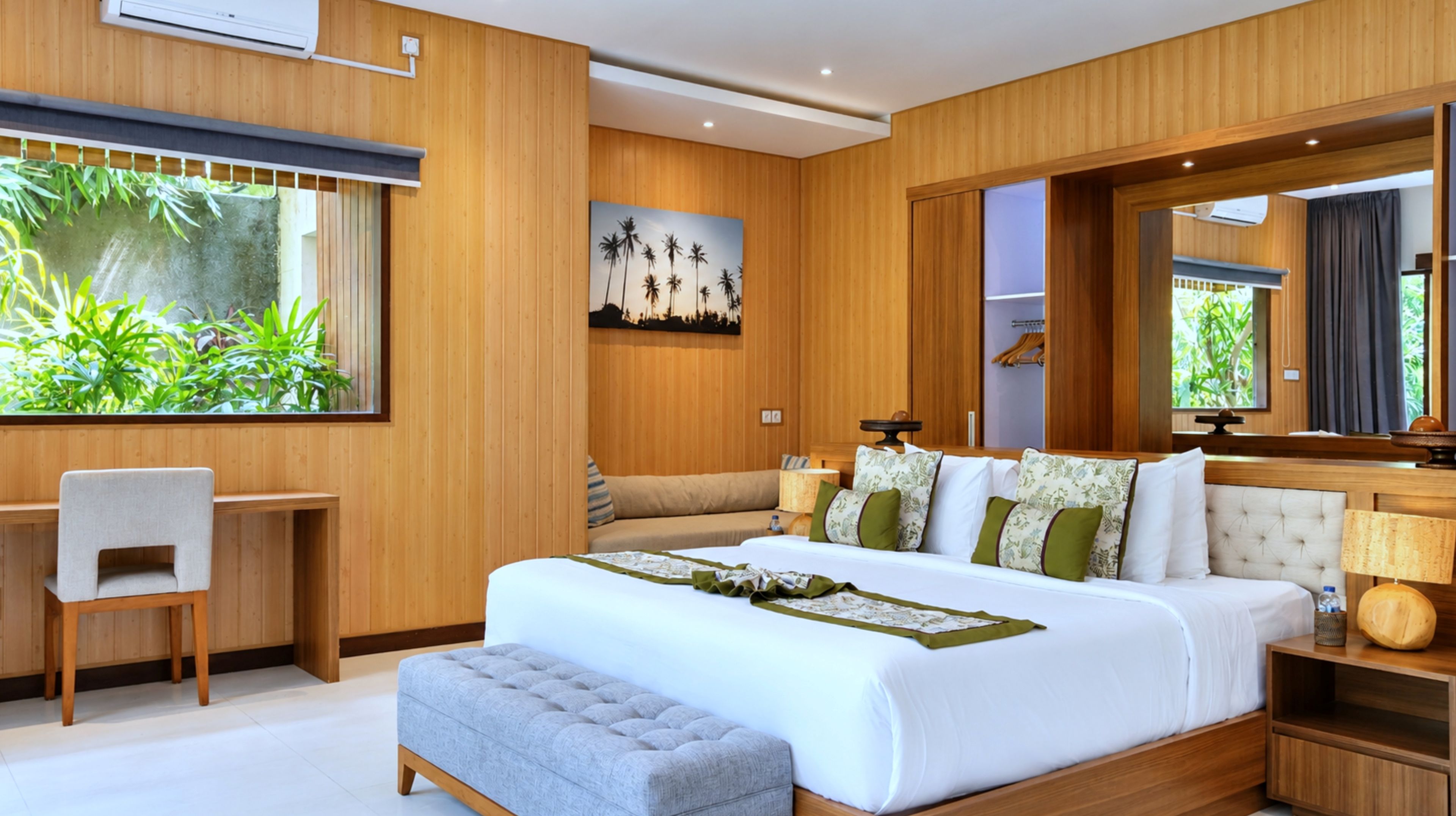 A modern bedroom with a large bed, a desk, and a view of greenery.