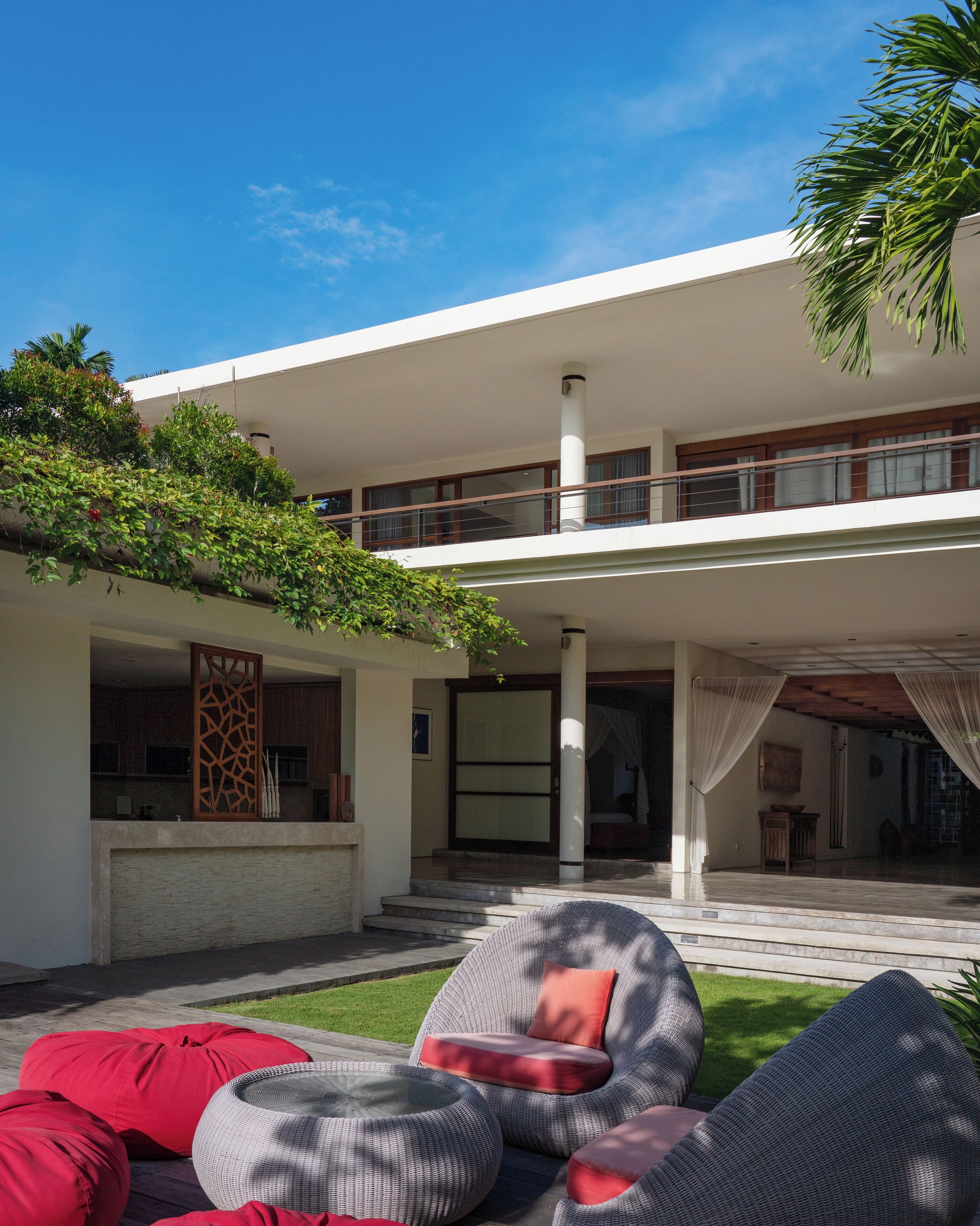 Une maison moderne dotée d’un patio couvert, d’un espace salon extérieur et d’un balcon donnant sur le jardin.