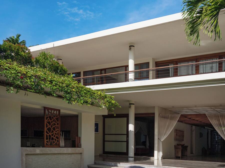 Une maison moderne dotée d’un patio couvert, d’un espace salon extérieur et d’un balcon donnant sur le jardin.