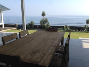 Een houten tafel met banken in een overdekt terras met uitzicht op de oceaan.