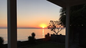 Sonnenuntergangblick von einer überdachten Außenbereits mit Blick auf ein Gewässer.