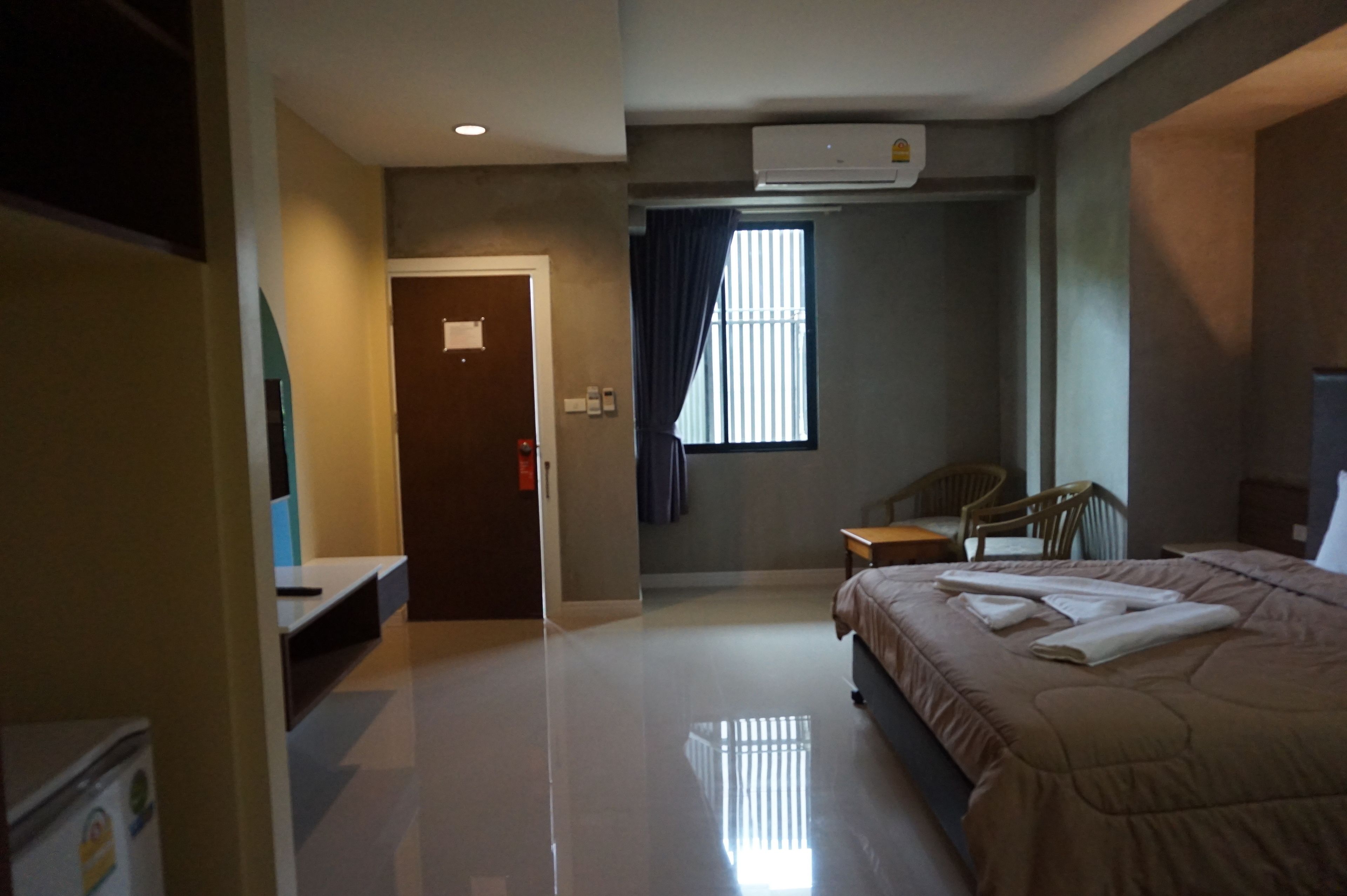 A hotel room with a bed, a desk, a chair, an air conditioning unit, and a window with curtains.