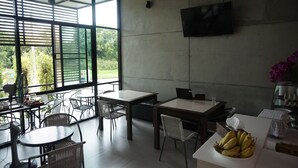 Un comedor moderno con amplios ventanales, mesas, sillas y un televisor de pantalla plana montado en la pared.