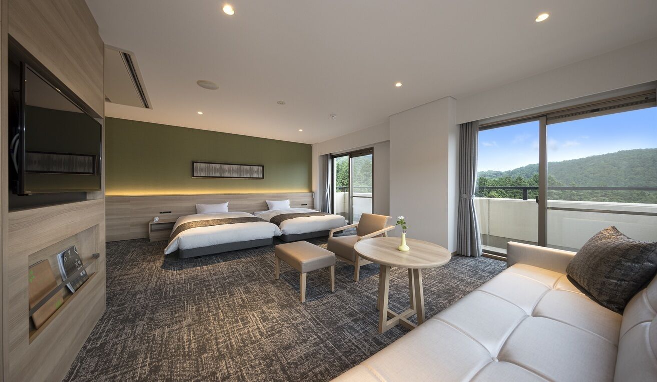 A hotel room with a bed, two bedside tables, a sofa, a small round table, and a TV.