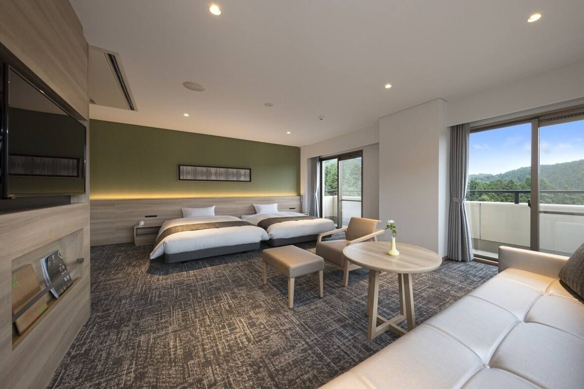 Una habitación de hotel con una cama, dos mesitas de noche, un sofá, una pequeña mesa redonda y un televisor.