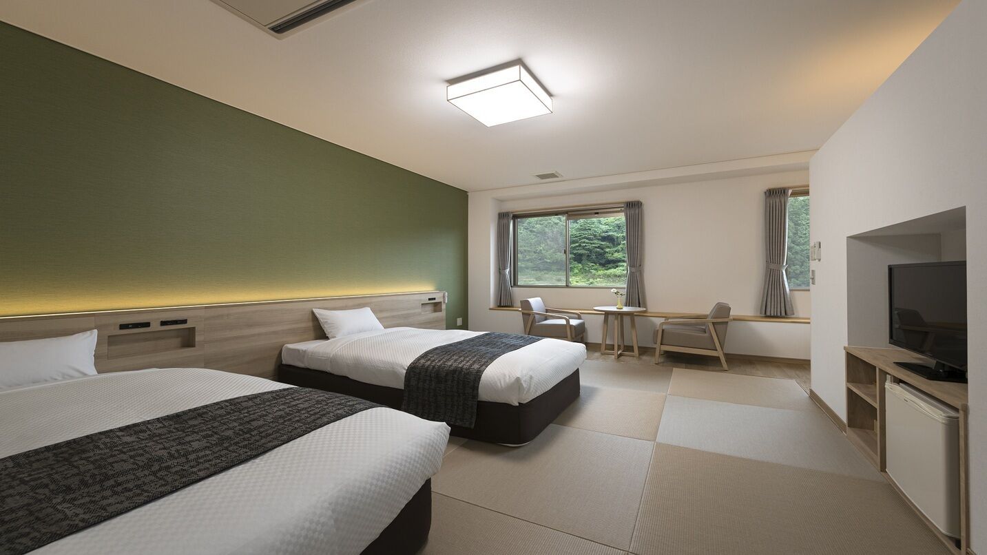 A hotel room with two beds, a desk, a chair, a TV, and a window with curtains.