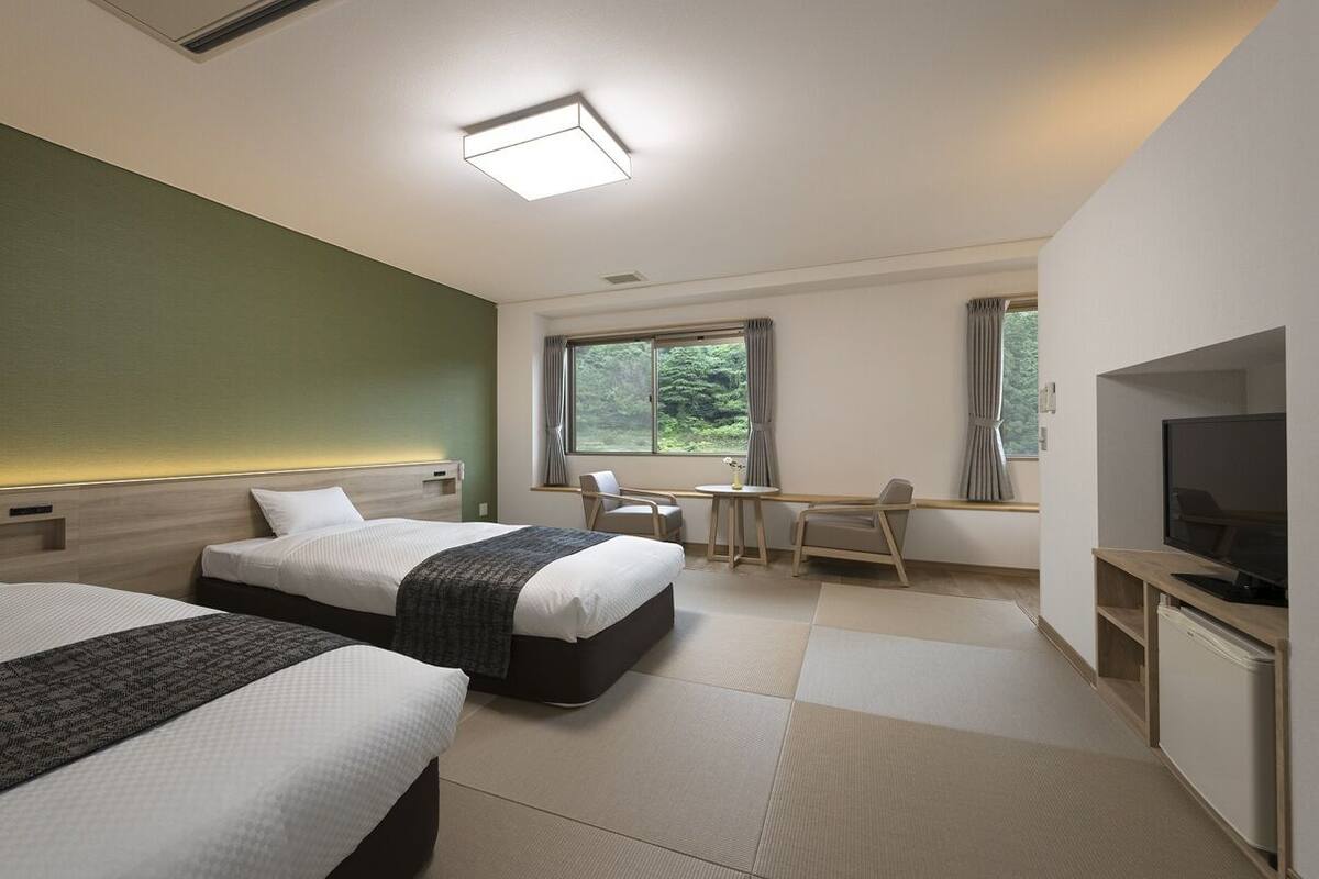 Una habitación de hotel con dos camas, un escritorio, una silla, un televisor y un ventanal con cortinas.