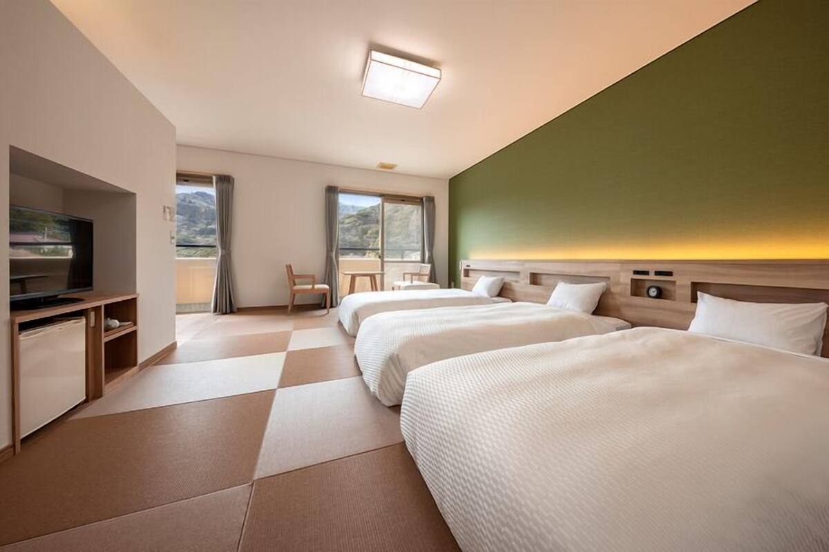 Habitación de hotel con dos camas, televisión, escritorio y vista al exterior.