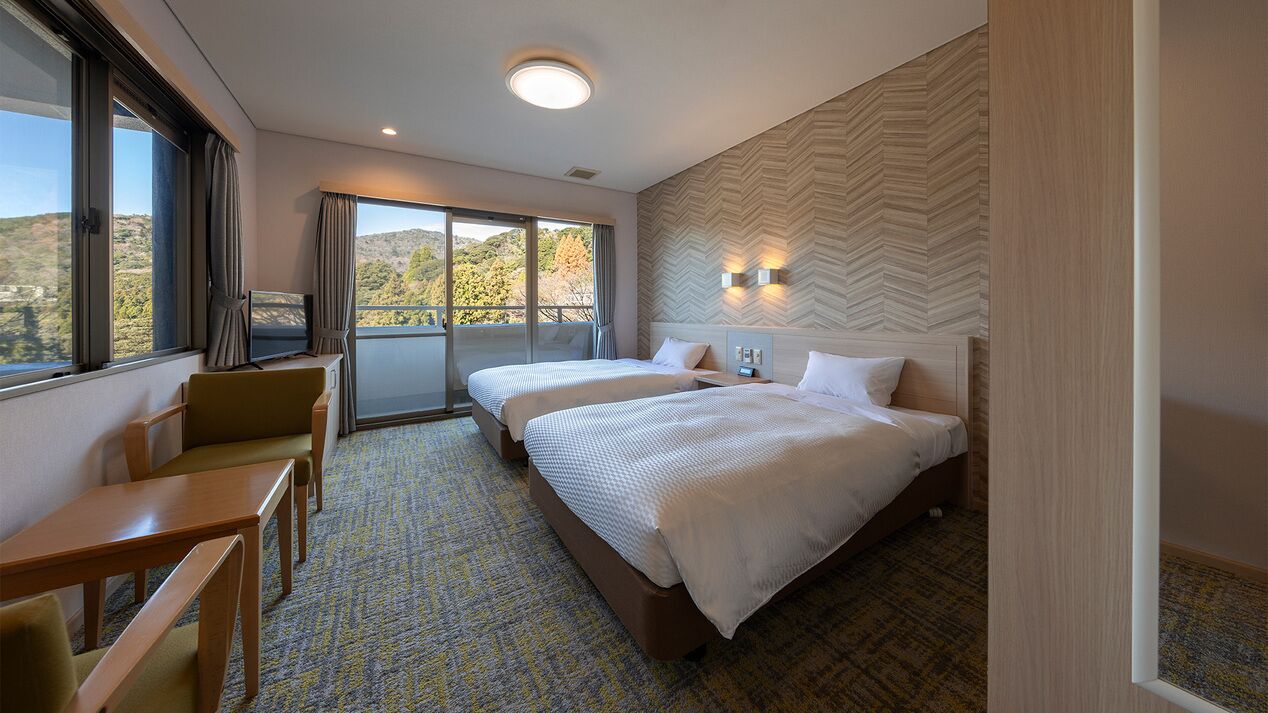 A hotel room with two beds, a desk, and a view of the outdoors.