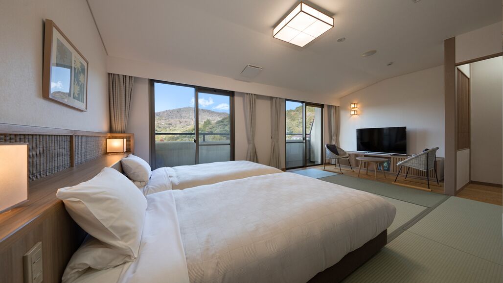 A hotel room with two beds, a TV, a balcony, and a view of the mountains.