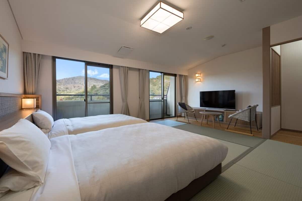 Habitación de hotel con dos camas, televisión, balcón y vistas a las montañas.