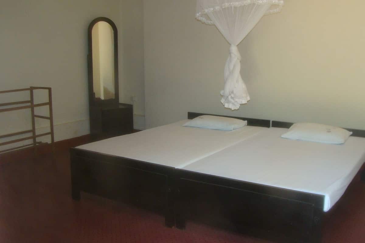 Quarto simples e limpo com uma cama de solteiro, mesa de cabeceira, espelho e mosquiteiro.