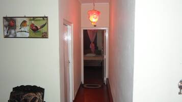 Un couloir étroit avec un plancher en bois, une porte sur la gauche et, au fond, un lit surmonté d’un baldaquin rose.